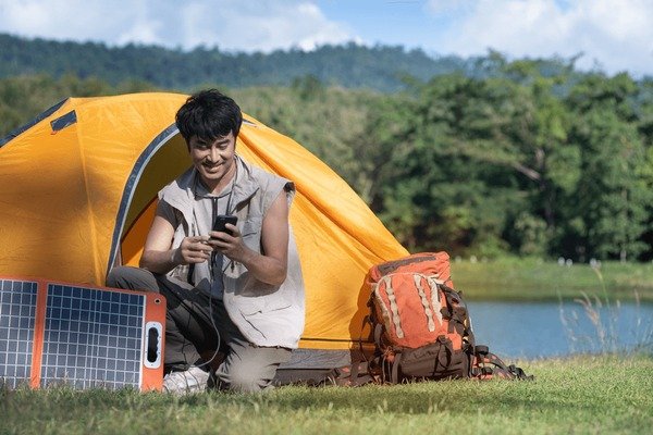 Traveler charging smartphone using a portable solar power bank while camping in 2025